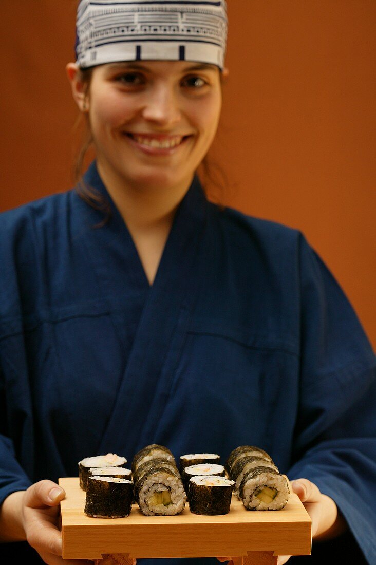 Woman in blue kimono serving maki-sushi