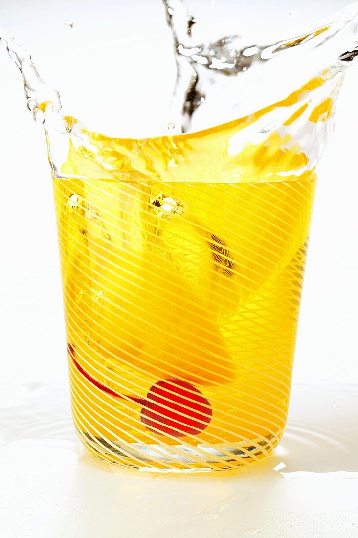 Tonic mit Zitrone und Cocktailkirsche spritzt aus dem Glas