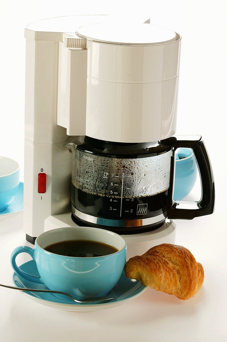 Kaffeemaschine, blaue Kaffeetassen und Croissant