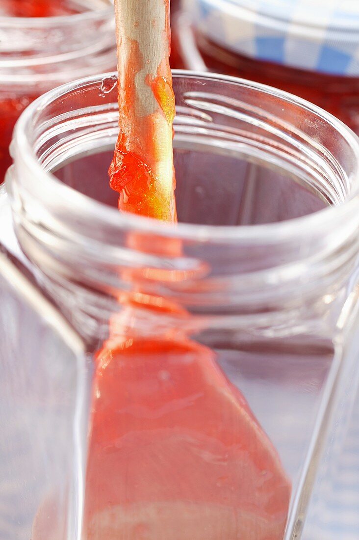 Kitchen spoon with strawberry jam in jam jar