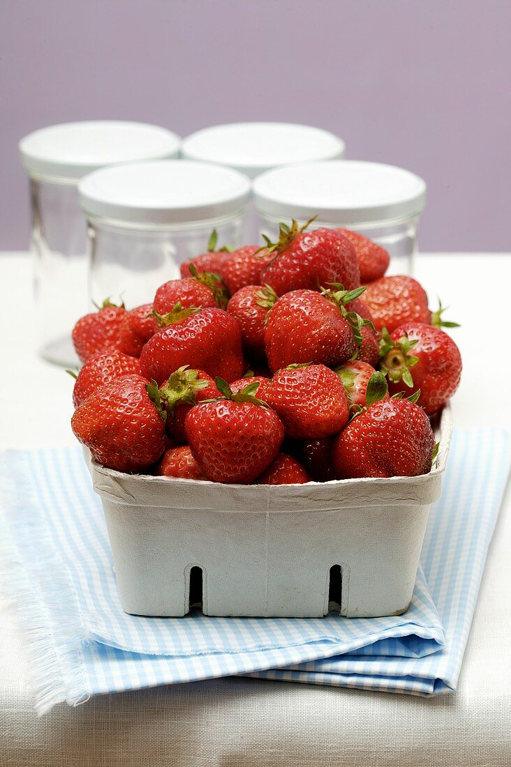 Fresh strawberries in cardboard punnet; jam jars