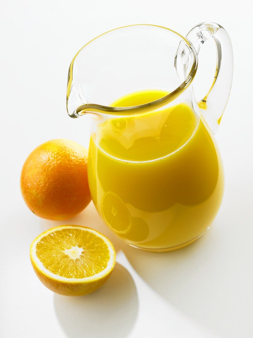 Orange juice in glass jug; fresh oranges