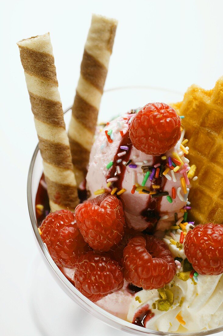 Eisbecher mit Himbeereis, Sahne, Waffeln und Zuckerstreuseln