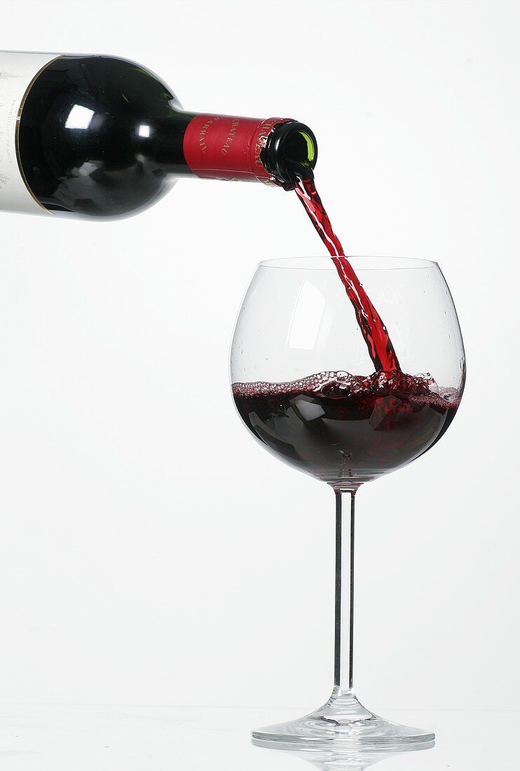 Rotwein aus Flasche in Glas gießen