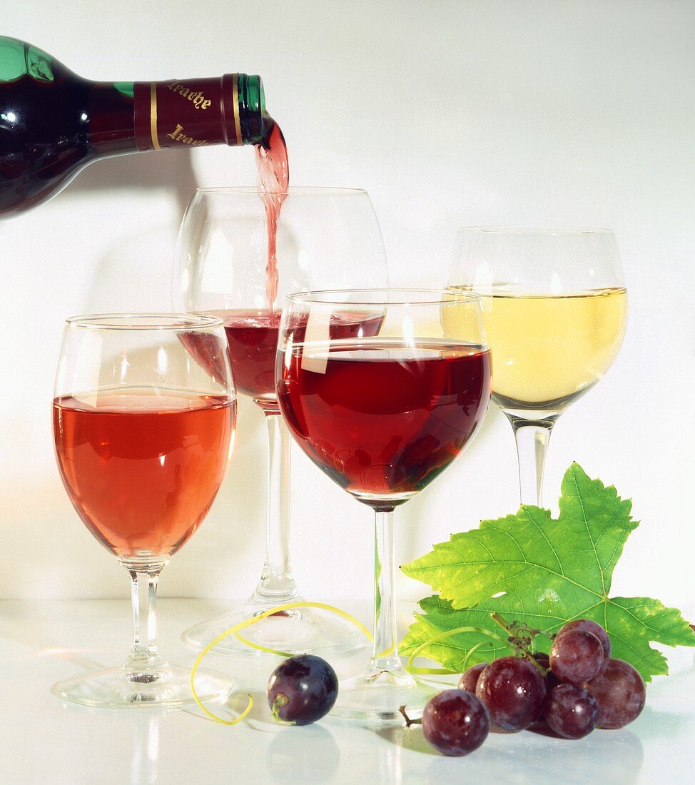 Pouring red wine; wine glasses; red grapes