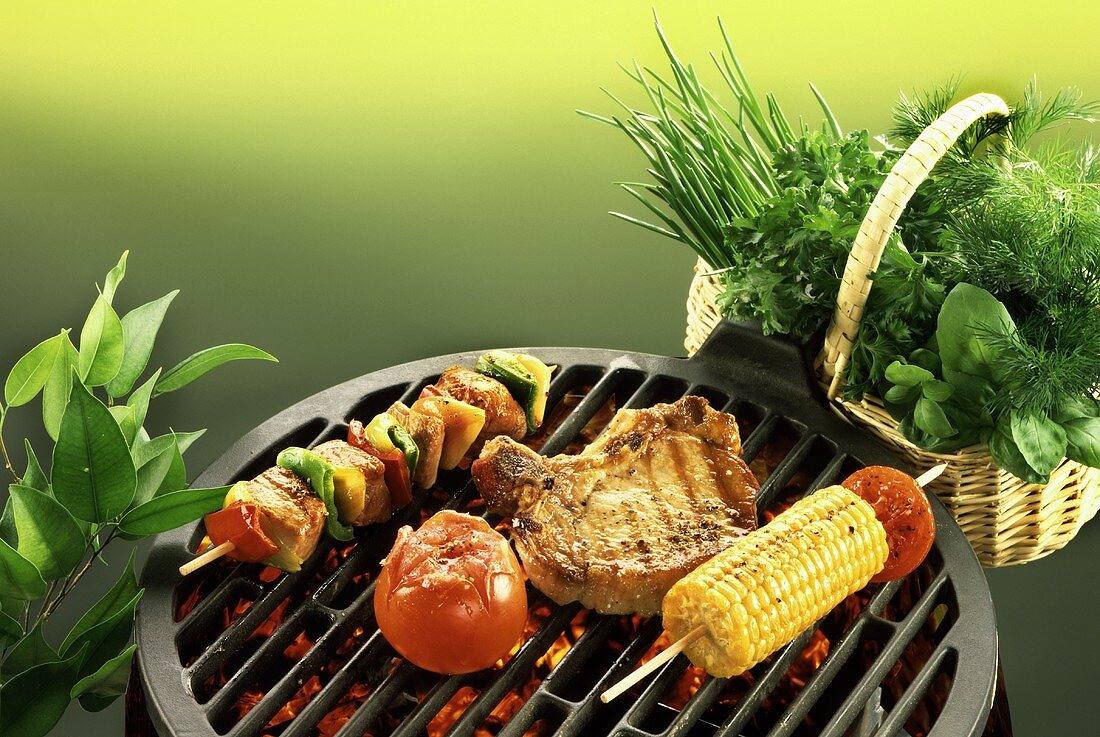 Chop, kebab, sweetcorn and tomato on barbecue; fresh herbs