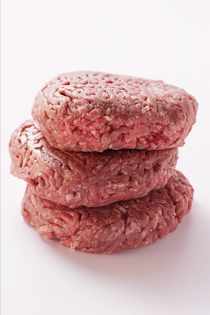 Three raw burgers in a pile