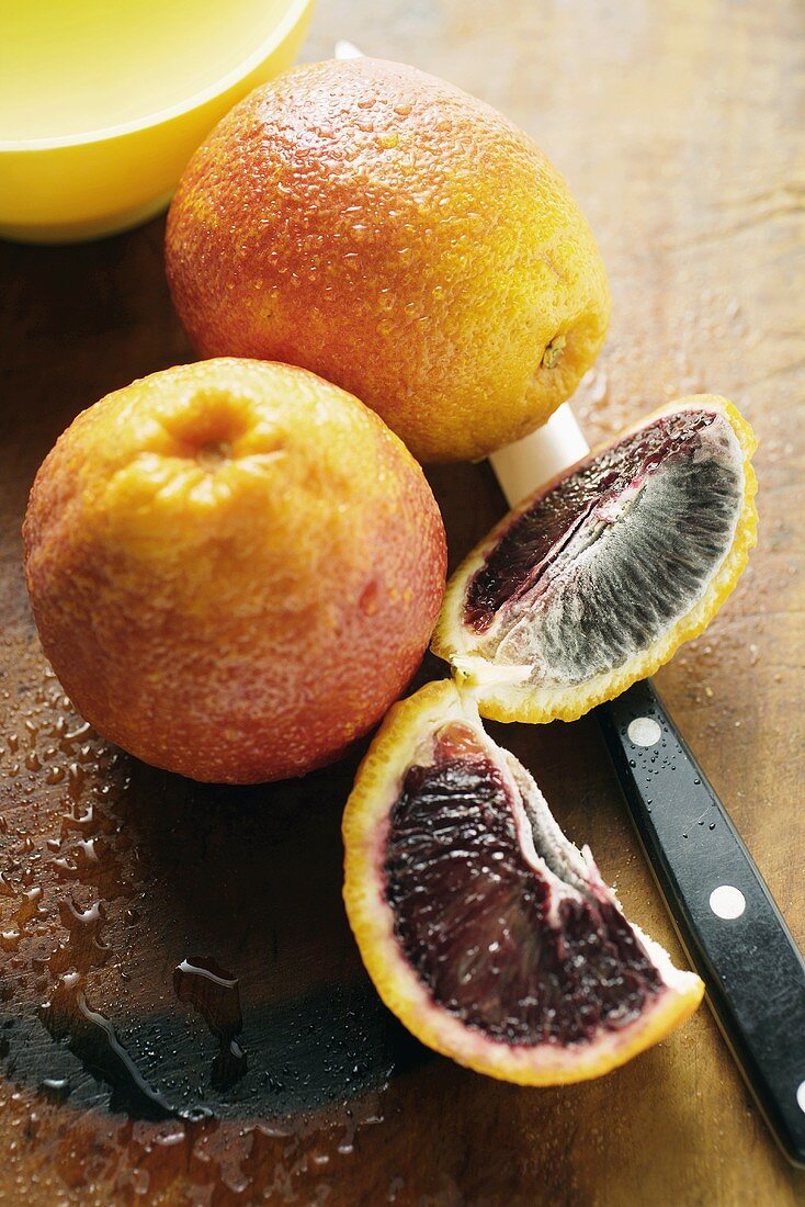 Blood oranges, whole and two wedges, on chopping board