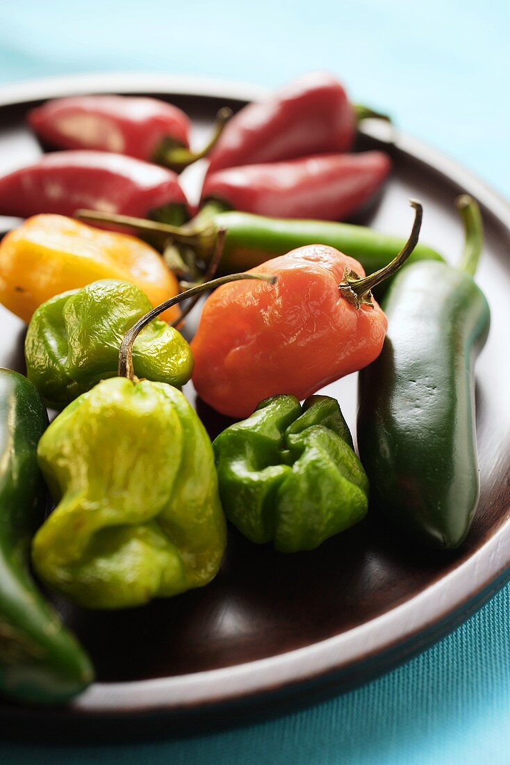 Various chili peppers on wooden plate