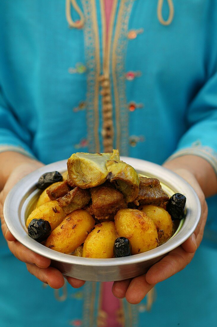 Person holding bowl of lamb ragout and potatoes (Morocco)