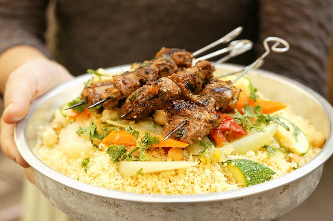 Person serving kebabs with vegetables and couscous