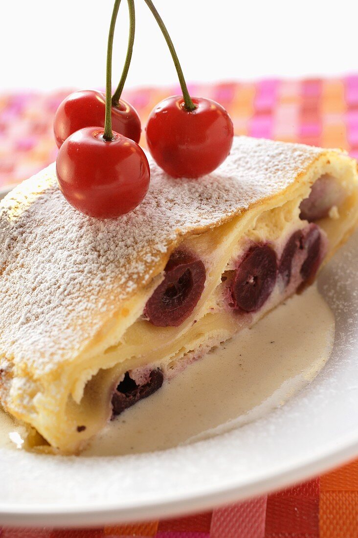 Piece of cherry strudel with icing sugar and fresh cherries