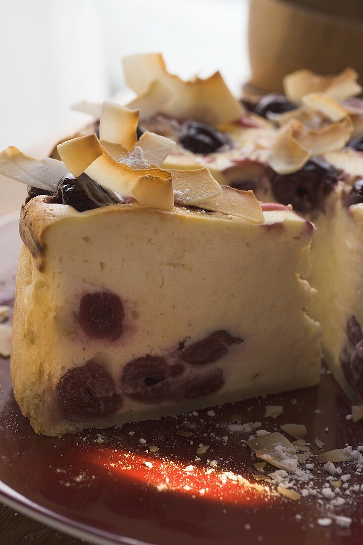 Cheesecake with cherries and coconut shavings, a piece cut