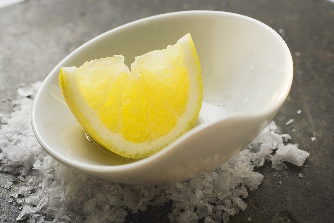 Lemon wedge with olive oil in a small bowl on salt
