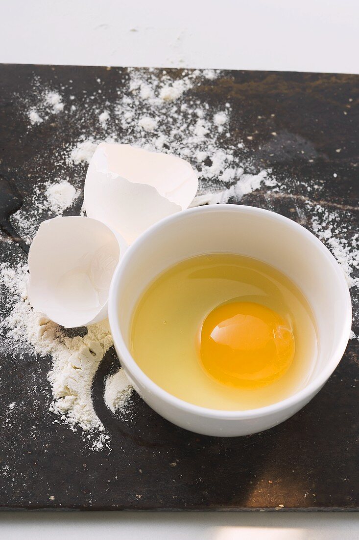 Aufgeschlagenes Ei, Eierschalen und Mehl