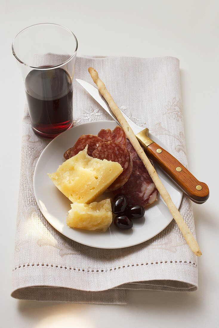 Salami, Käse, Oliven und Grissini auf Teller, Glas Rotwein
