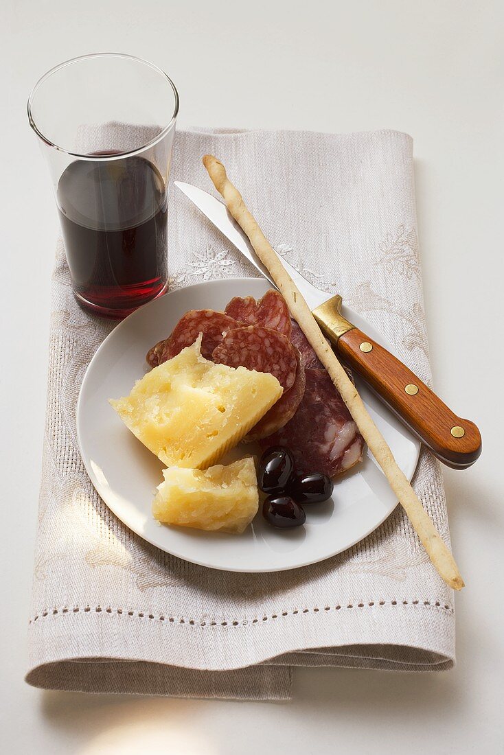 Salami, cheese, olives & grissini on plate, glass of red wine