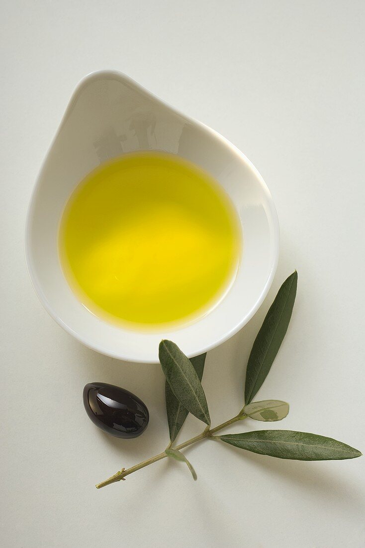 Olivenöl in Schale, daneben Olive und Olivenzweig