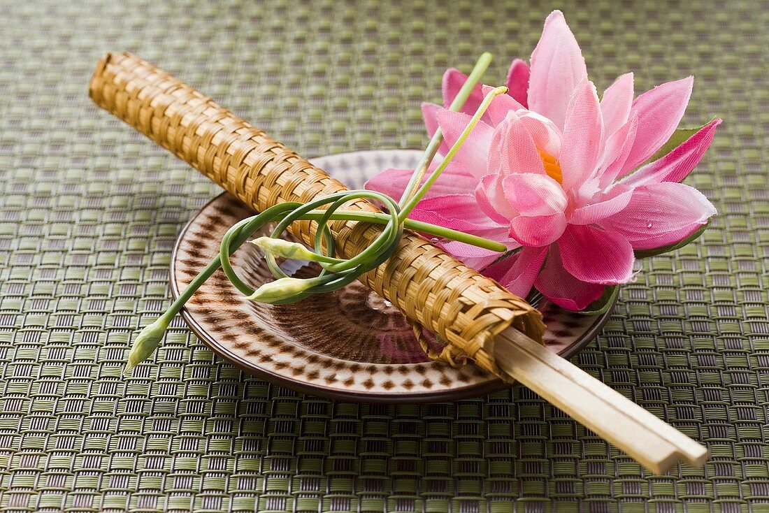 Chopsticks in woven wrapper with water lily on plate