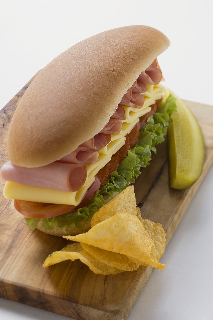 Sub sandwich with crisps and gherkin on chopping board