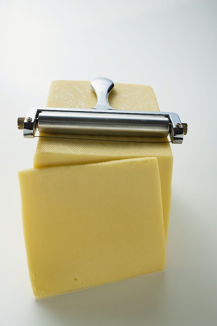 Semi-hard cheese with a slice cut and a cheese cutter