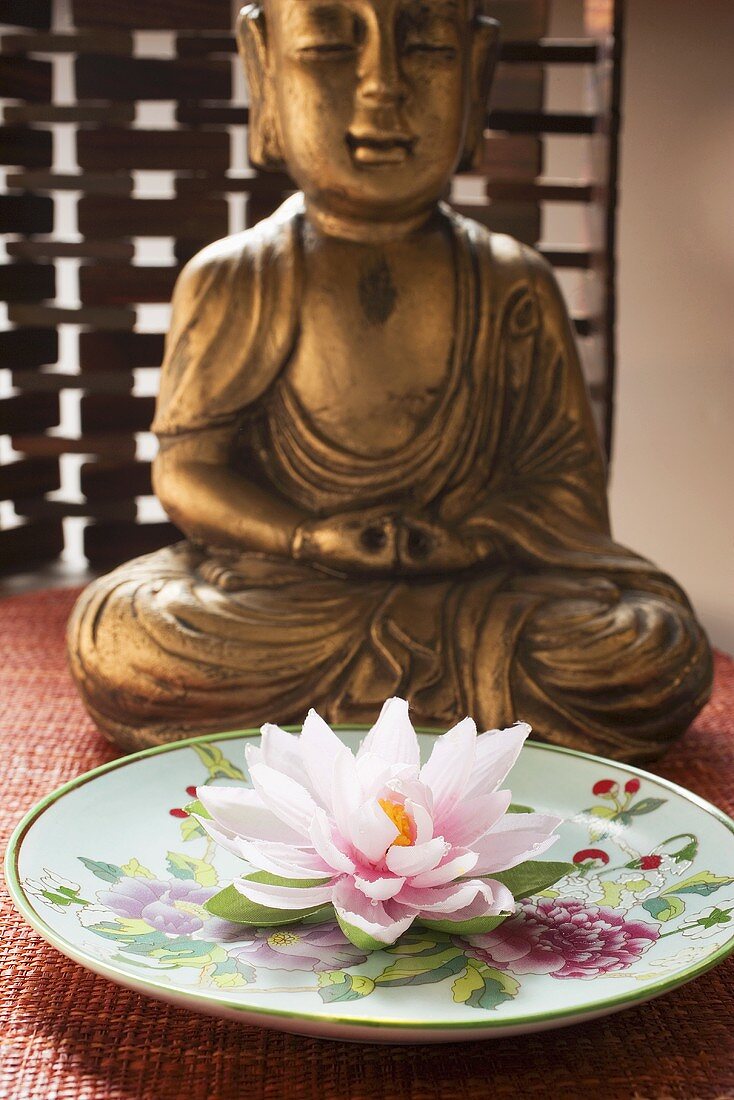 Asiatischer Teller mit Seerose vor Buddhastatue