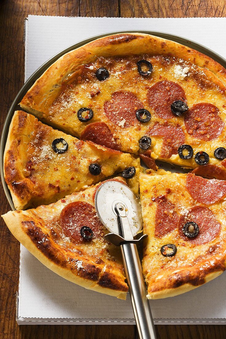 Pizza mit Salami, Käse und Oliven mit Pizzaschneider