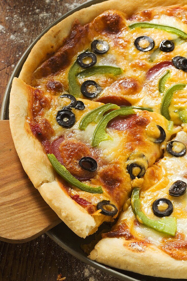 Pizza mit Käse, Salami, Paprika und Oliven, angeschnitten