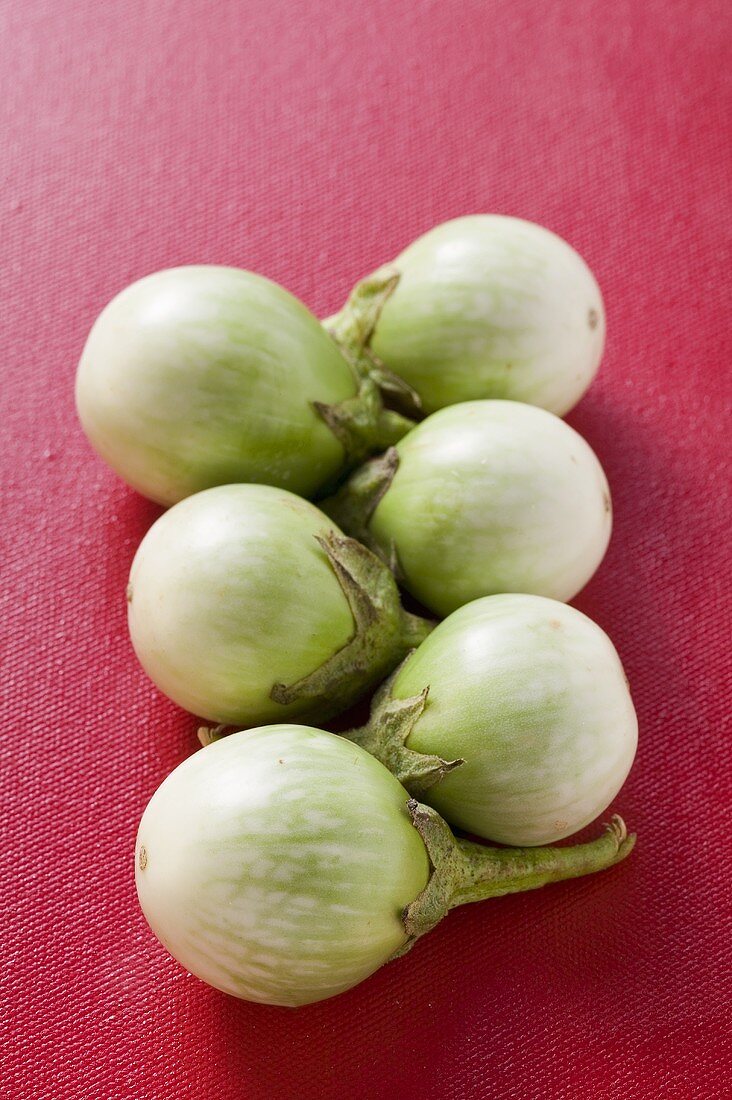 Green baby aubergines on red background