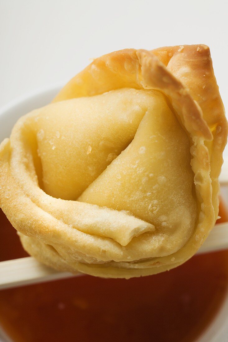 One deep-fried wonton with sweet and sour sauce (close-up)