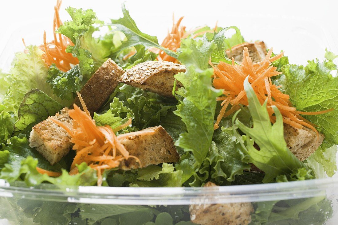 Salad leaves with carrots and croutons in take-out box