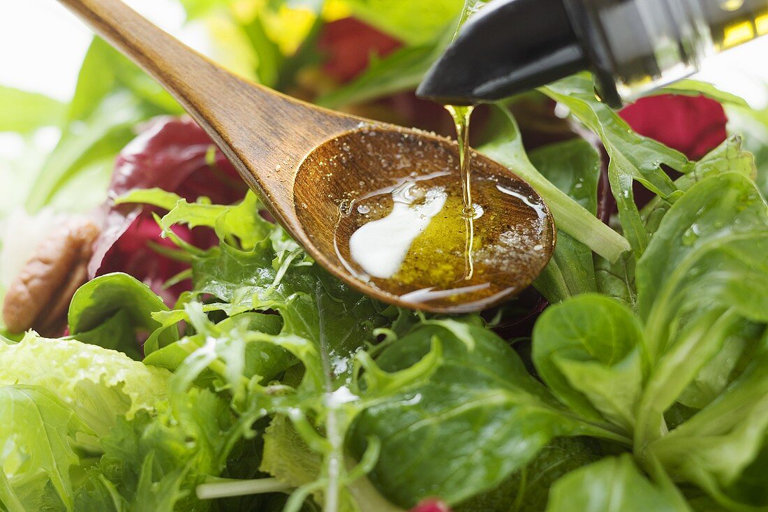 Pouring olive oil into wooden spoon above salad leaves