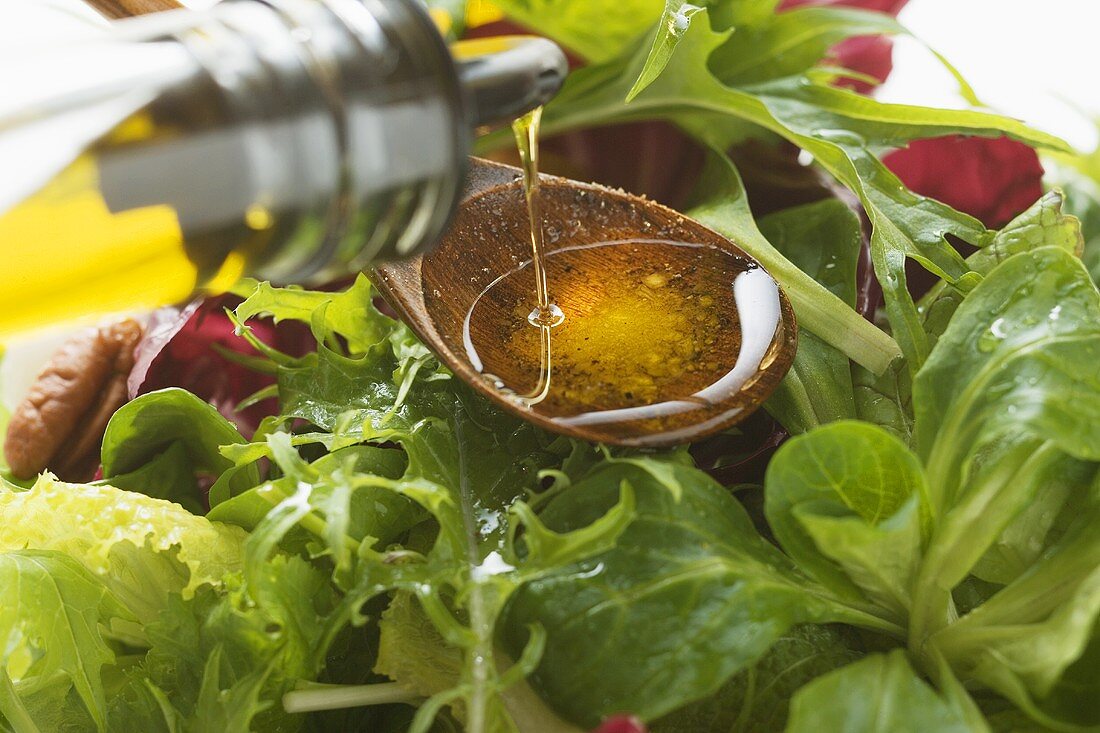 Pouring olive oil into wooden spoon above salad leaves