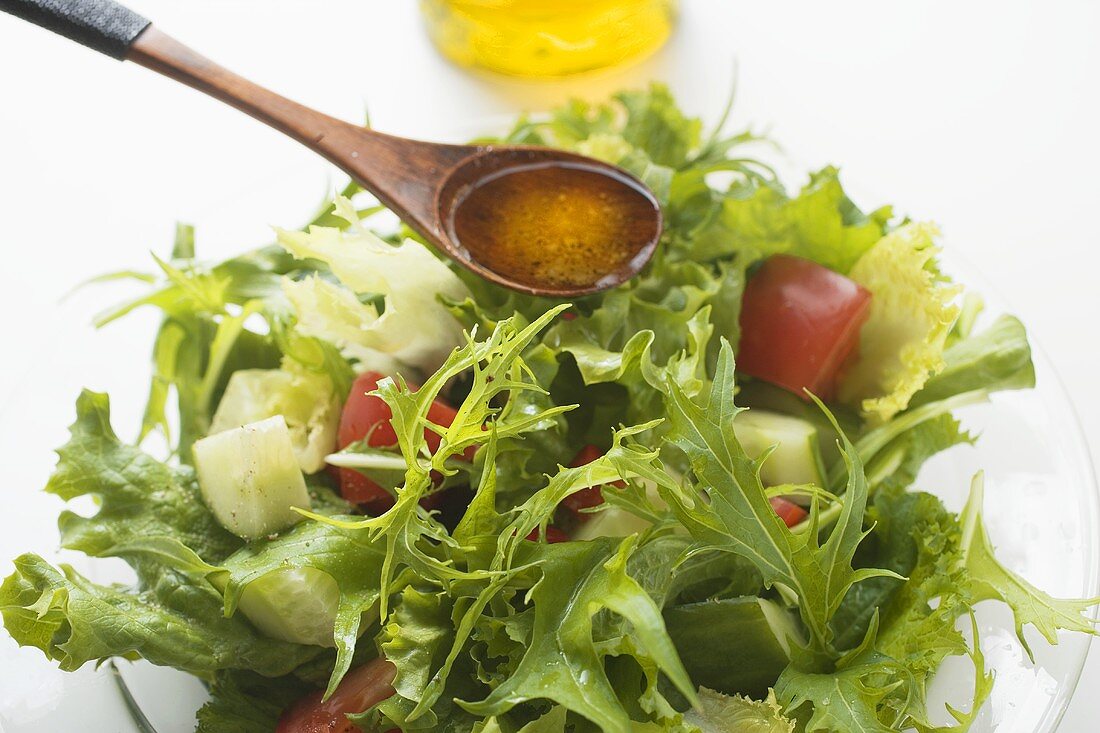 Olive oil in wooden spoon above salad leaves