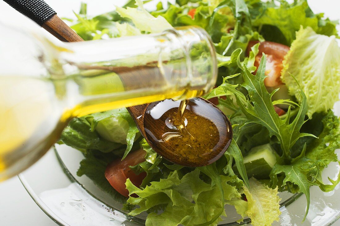 Olivenöl auf Kochlöffel über Blattsalat gießen