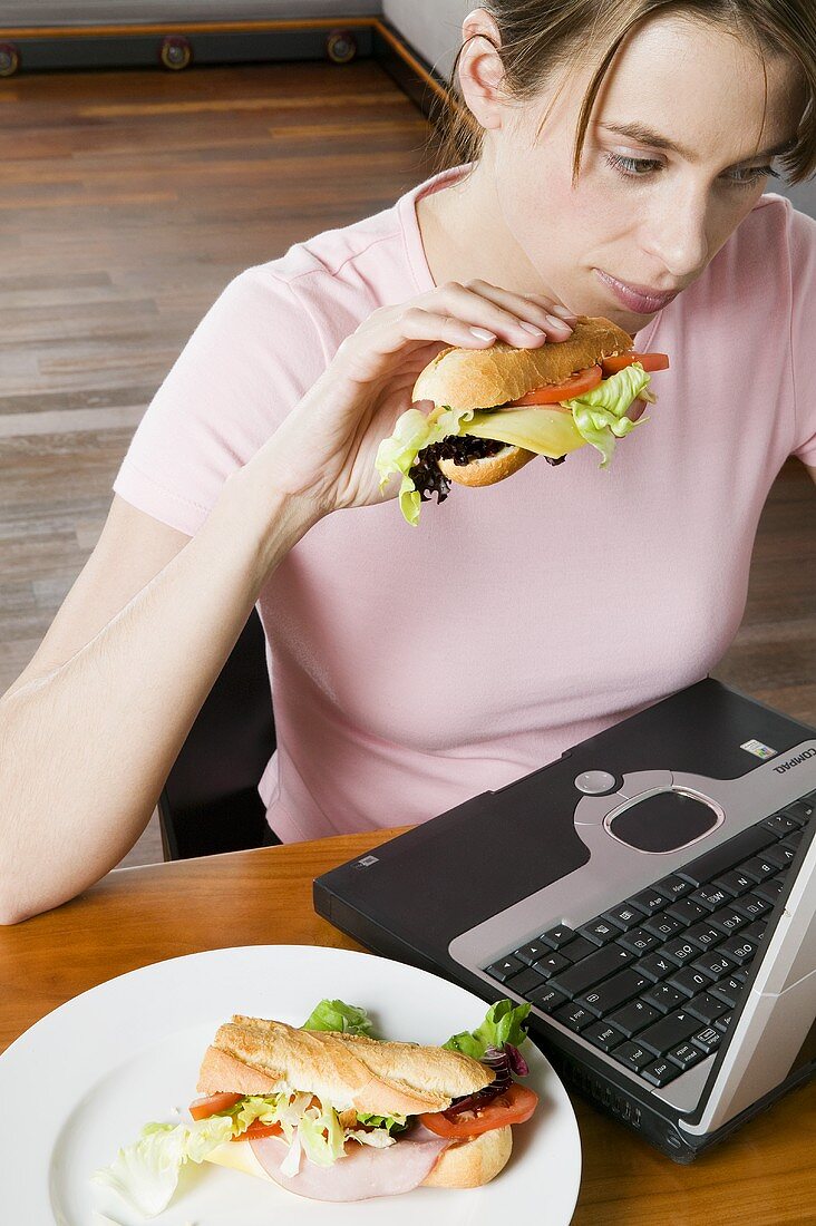 Junge Frau isst Sandwich bei der Arbeit am Computer