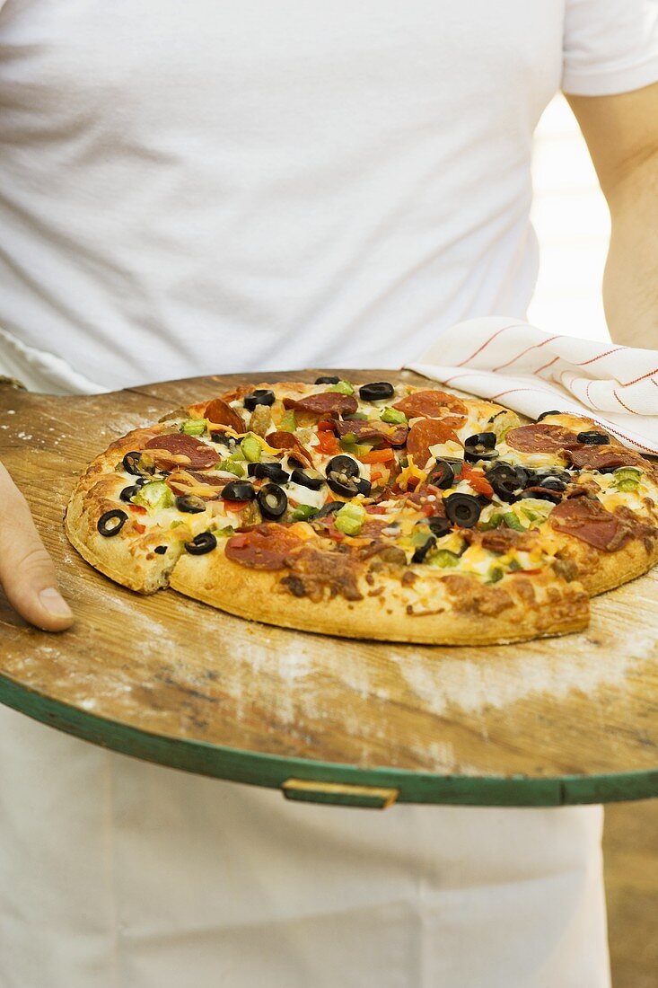 Person hält Pizza mit Peperoniwurst, Paprika und Oliven