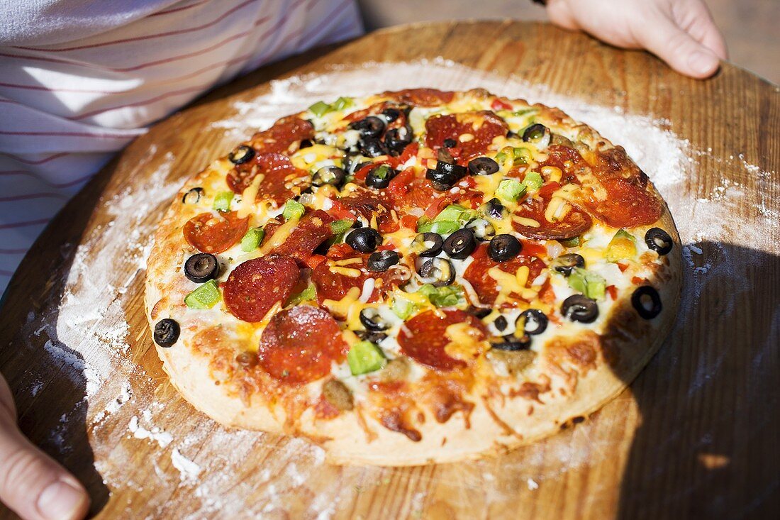 Hände halten Pizza mit Peperoniwurst, Paprika und Oliven