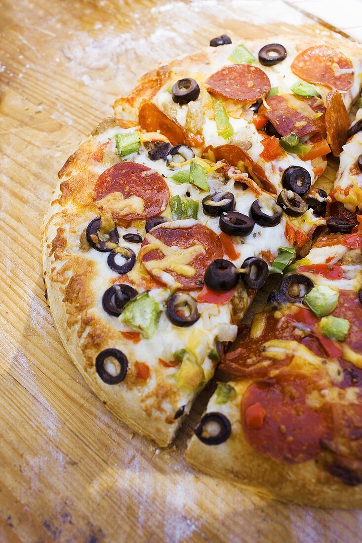 Pizza mit Peperoniwurst, Paprika und Oliven auf Holzteller