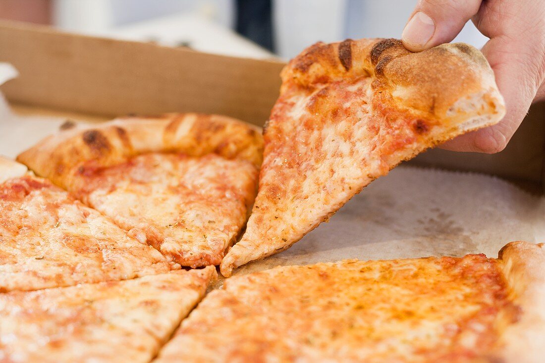 Hand nimmt Stück Pizza Margerita aus Pizzakarton