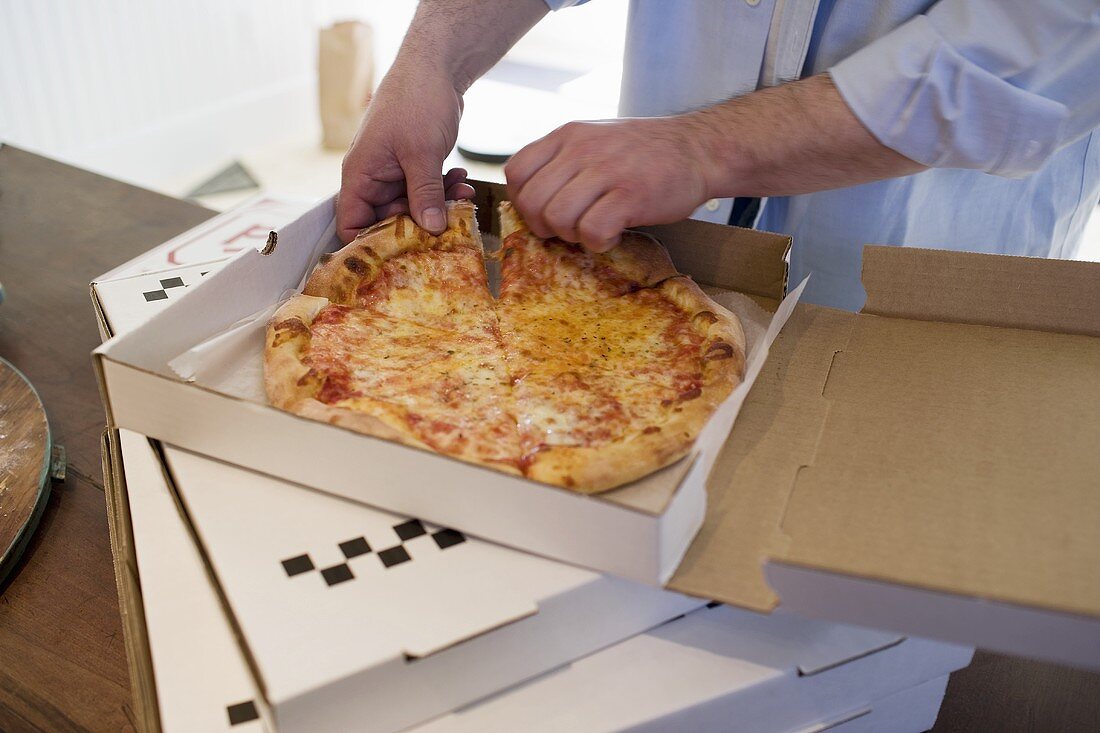 Mann nimmt Stück Pizza Margerita aus Pizzakarton