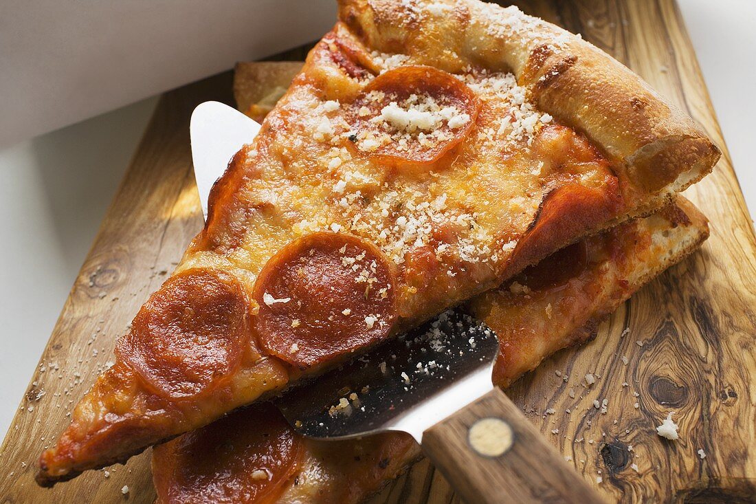 Zwei Stücke Peperoniwurst-Pizza mit Heber auf Holzbrett