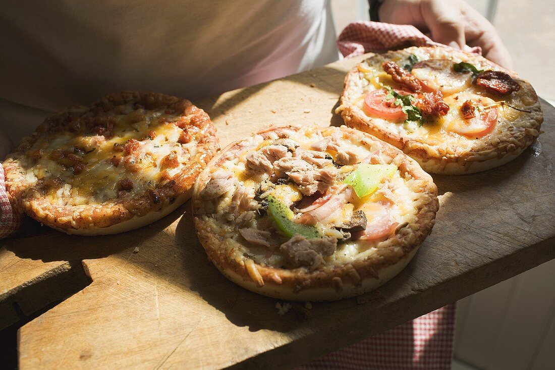 Person hält Holzbrett mit drei verschiedenen Minipizzen