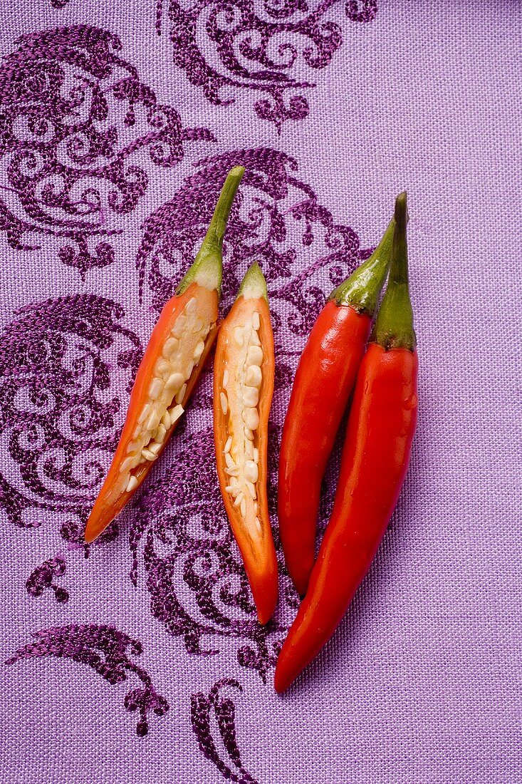 Red chili peppers on purple fabric, one cut open