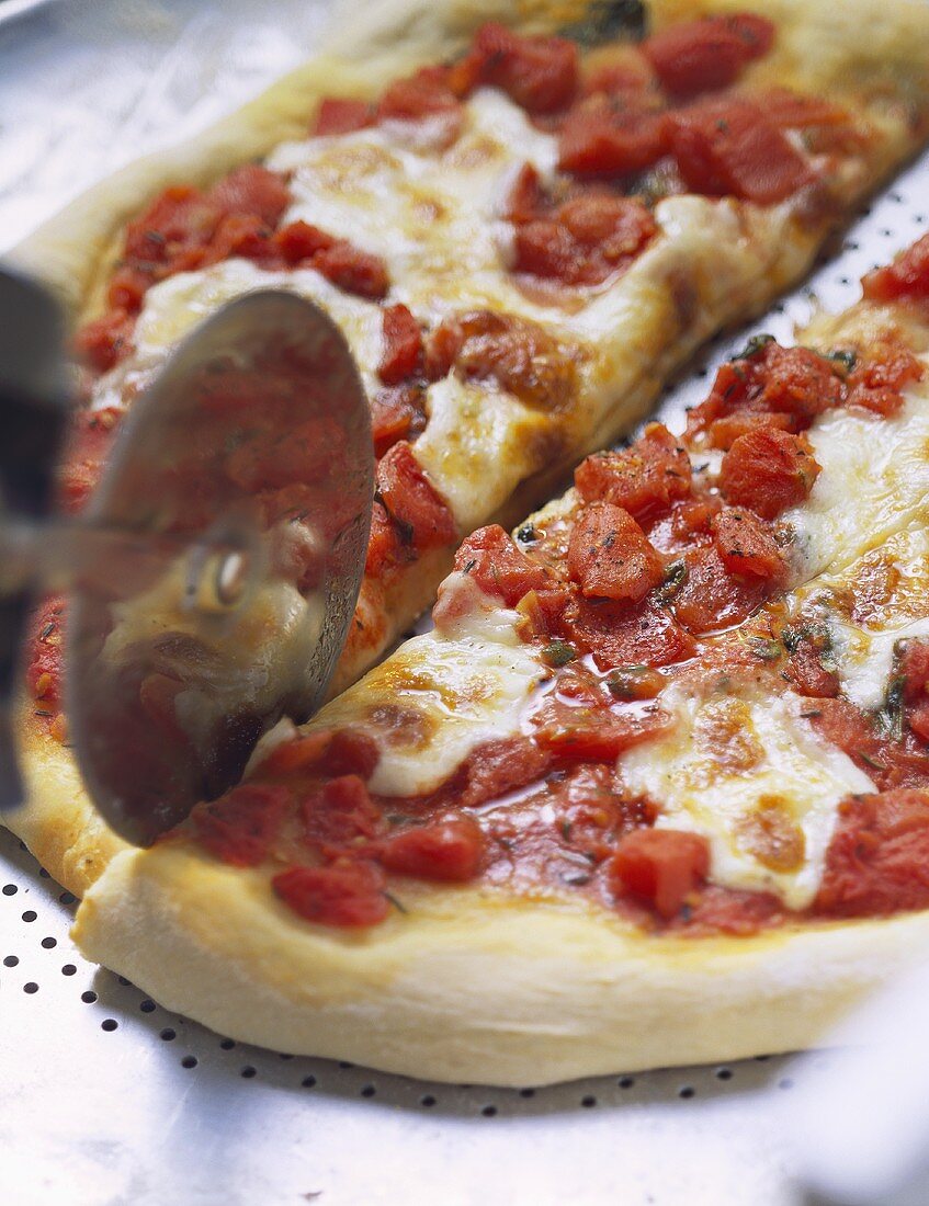 Pizza mit Tomaten und Mozzarella mit Pizzaschneider zerteilen