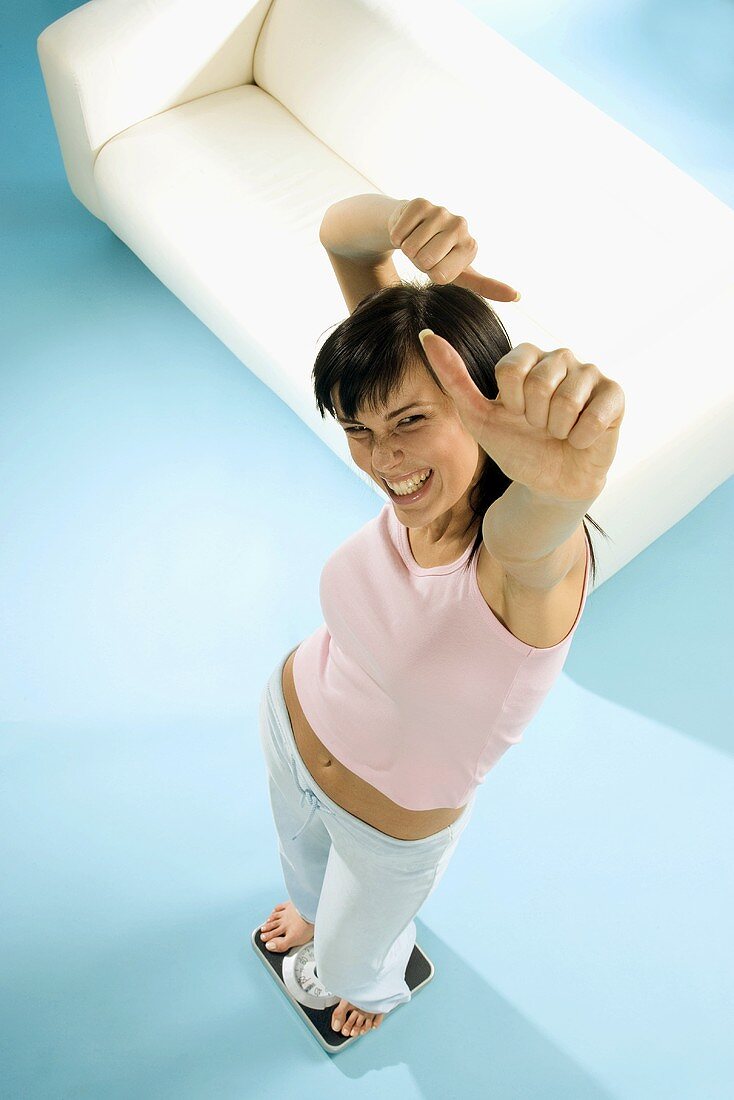 Young woman standing on scales, looking triumphant