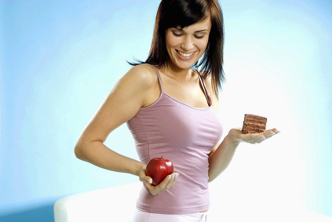 Young woman holding piece of cake and apple in her hand