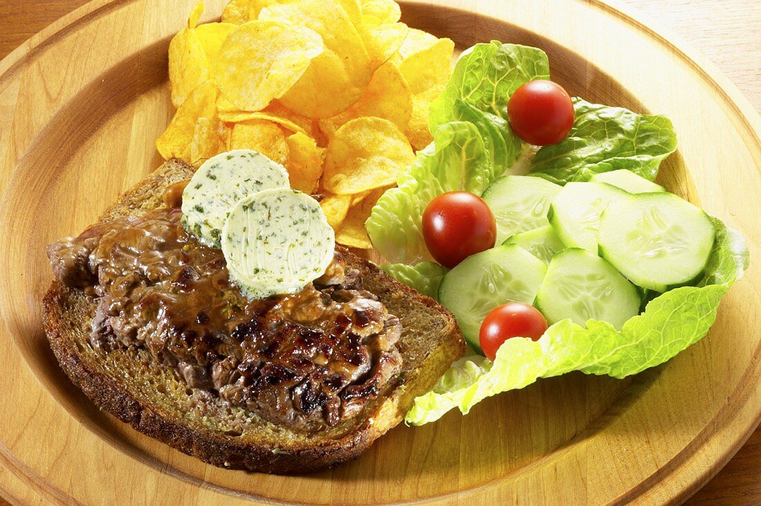 Steak mit Kräuterbutter auf Brot, Kartoffelchips und Salat
