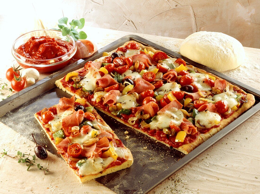 Pizza mit Gemüse und Schinken auf dem Blech