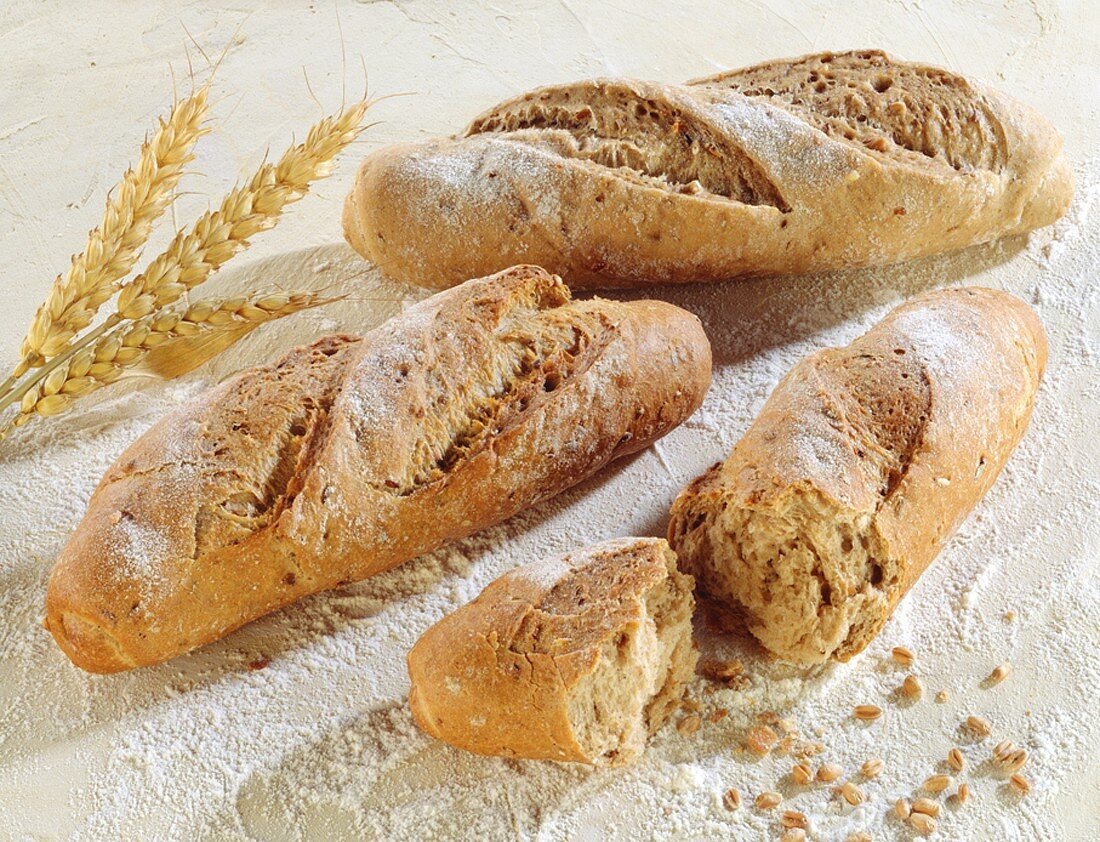 Three white bread sticks, beside wheat grains and ears